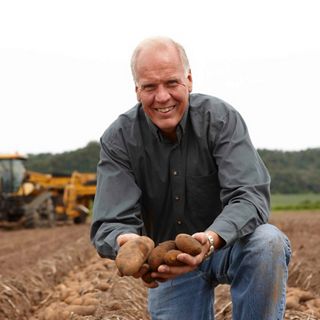 A man kneeling in a plowed farm field holding potatoes.