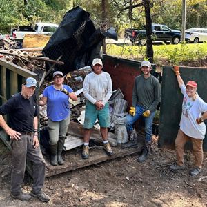 Five people stand around a dumpster full of garbage.