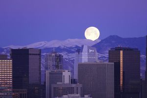 A huge moon rising over snow-capped mountains behind the Denver skyline.
