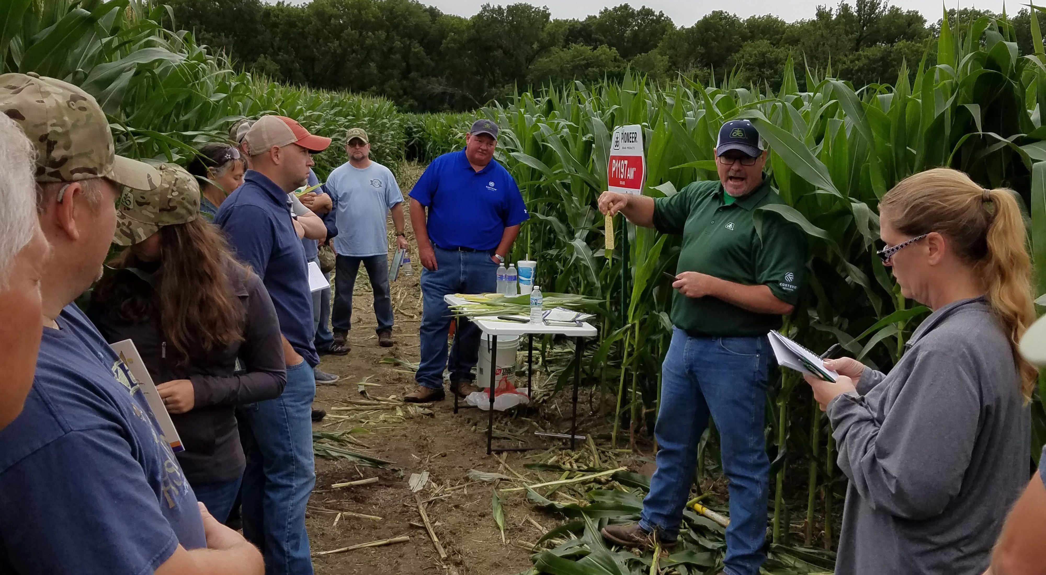 A farmer explains corn in a cornfield as a group of veterans listen.
