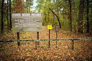 A sign reading Lennox Woods Preserve stands in an open area within dense forest.