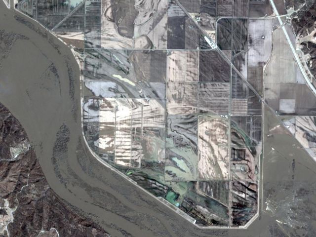 Satellite image of a flooded river that is held within the bounds of a levee.