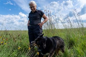 A woman looks down at a dog in a field.