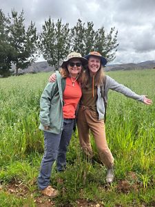 Two people standing together in a field of oats.