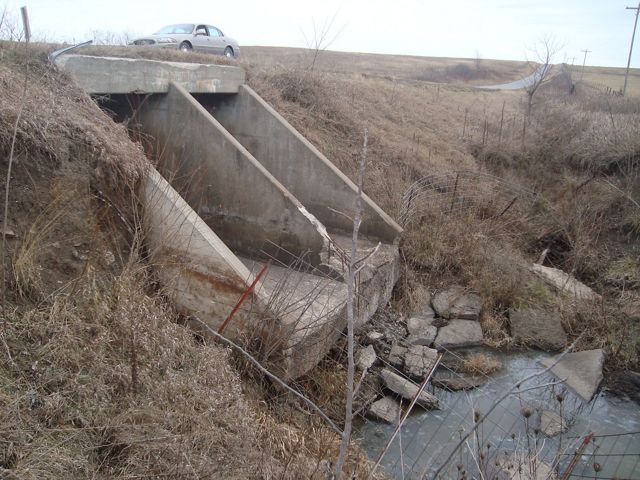A concrete culvert is perched about 5 feet above a stream. 