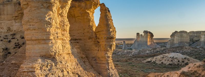 Rock formations climb toward a bright blue sky. A valley containing native shrubs can be seen between them.