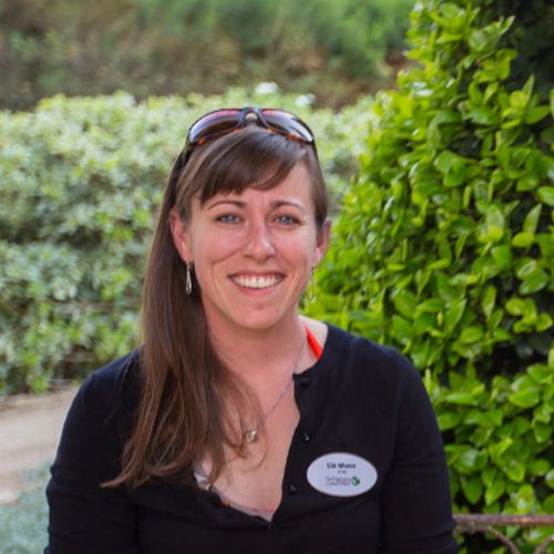 Liz Munn smiling at the camera in front of green trees