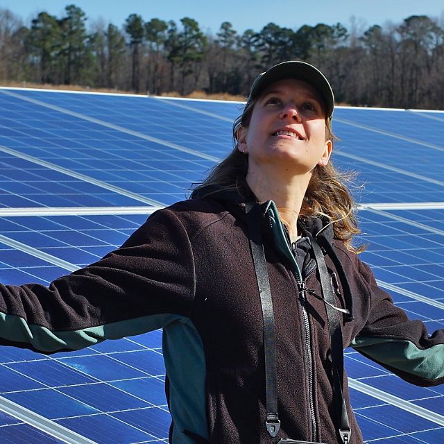 Liz Kalies stands in front of a large solar panel.