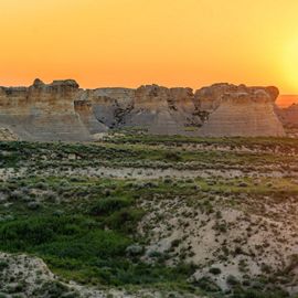 A view of Niobrara chalk formations and low scrubland from the Overlook Trail at Little Jerusalem Badlands State Park in Kansas at sunset.