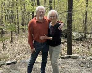 A smiling couple in a wooded setting.