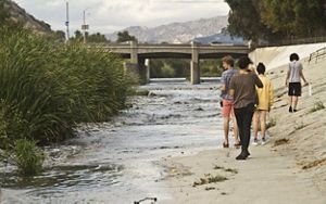 People walking on the concrete next to the LA River. 