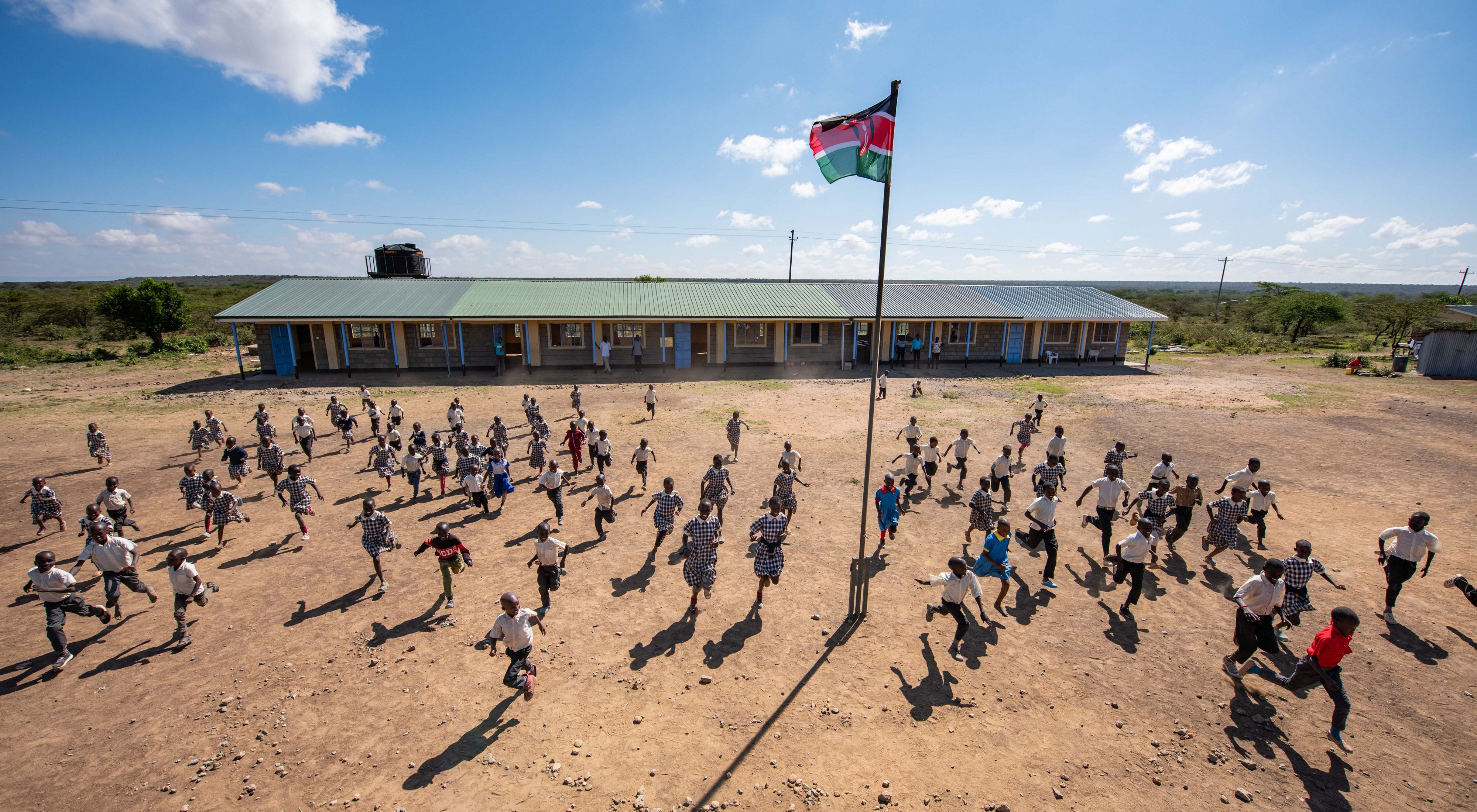 Dozens of children running through a dusty schoolyard