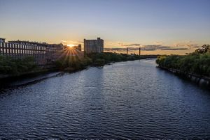 The Merrimack River at dusk lined by old mill buildings on one side and trees on the other.