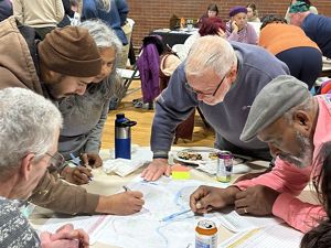 A group of Lowell residents gather around maps of the city spread on a table with pens in hand to provide input on flooding and heat.