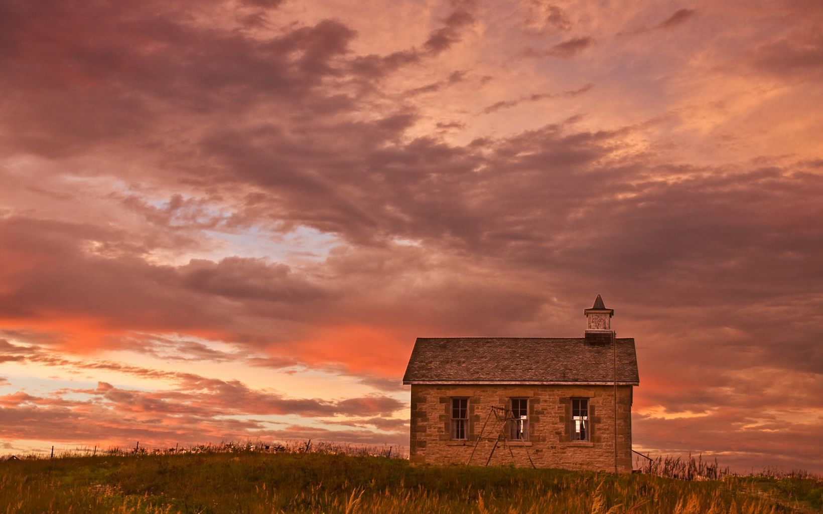 Small stone school house sits alone in a field.