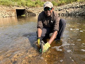 A man kneels in the water and holds a fish.