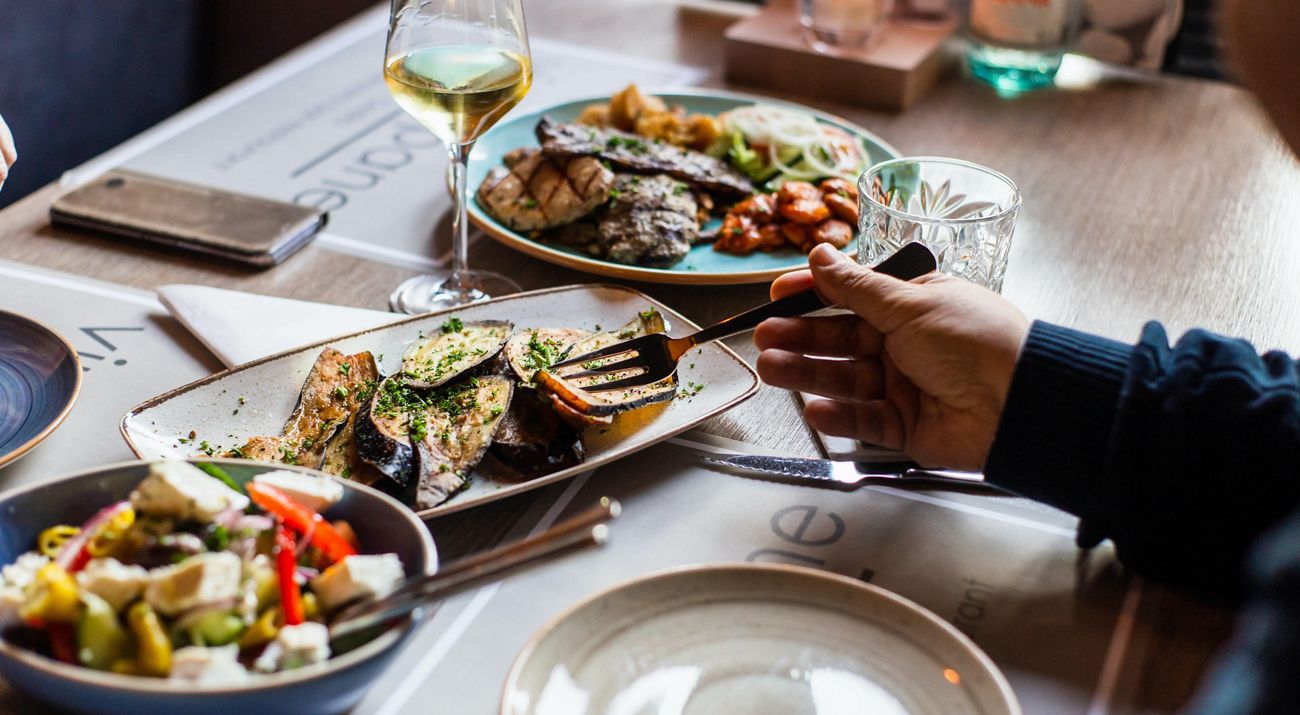 a person's arms pictured sitting at a dinner table with a variety of food on the table.