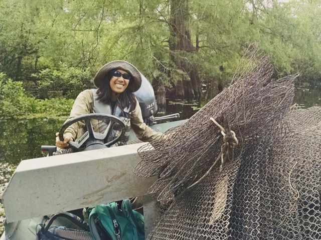 A woman in a hat steers a boat while holding a net.