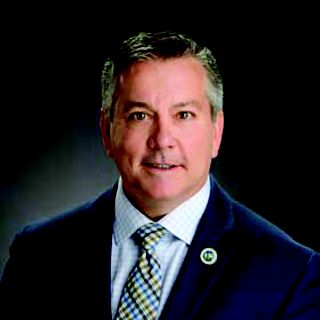 A man in a dark suit smiles at the camera.