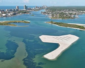 An aerial image features blue and green waters surrounding a sandy island.