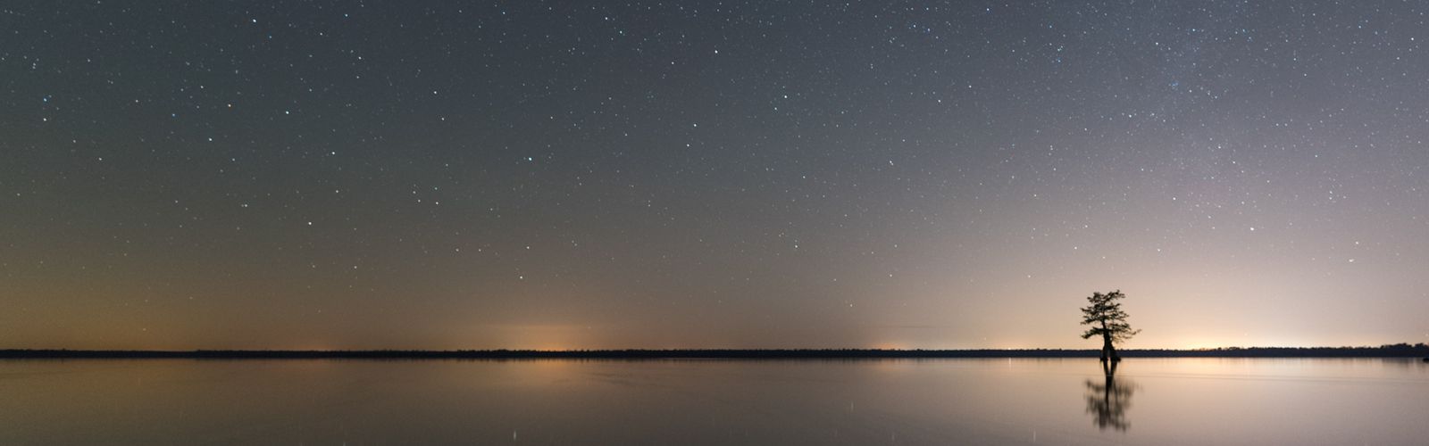 Twilight on a body of water with the sun just below the horizon and the stars visible.