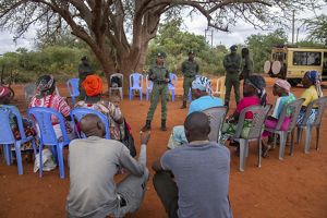 A group of people sit in a circle to speak with several park rangers, standing in the middle of the circle.