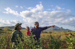 Two people, one holding a child in their arms, stand in a field of crops.