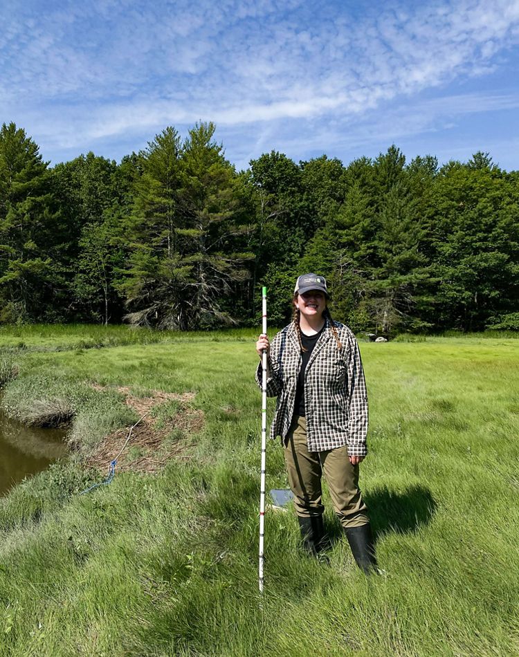 A woman standing in a saltmarsh near a creek.