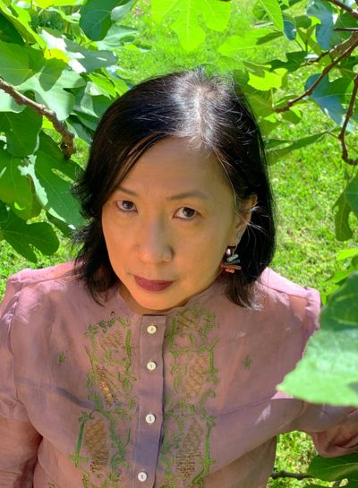 Headshot of poet, Luisa A. Igloria, posing in front of bright green leaves.