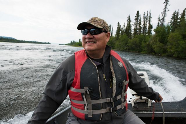 first nation man with sunglasses on a boat through a river surrounded by spruce forest in canada's boreal forest