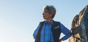A woman wearing a vest with a Nature Conservancy logo looks out into the distance.