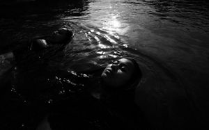 A black and white picture of a woman floating on a river, with just her face emerging. 