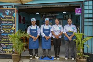 Cuatro personas con uniforme culinario posan en la puerta de un restaurante colorido.