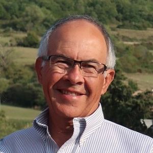 Retrato de Joseph Quiroz, en un fondo natural, con pelo cano, gafas y camisa. 