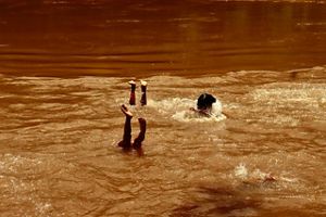 Two kids playing on the water of a river, on a picture with dominant orange tones. 
