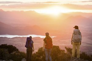 Tres personas admiran el atardecer desde la cima de una montaña.