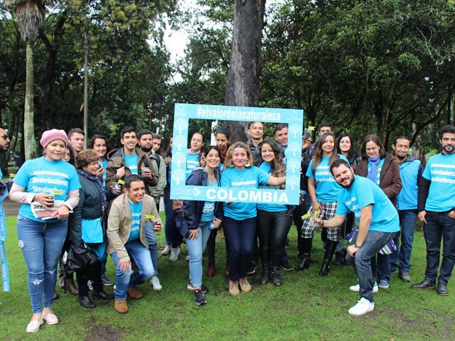 Around 20 smiling people pose in neon blue shirts with #TheValueOfNature, some holding a sign reading "Colombia" 
