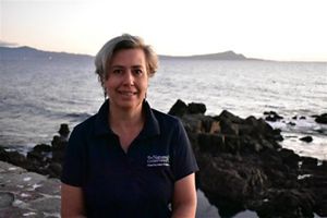 Una mujer con una camisa azul está de pie junto al mar, con las olas rompiendo suavemente al fondo.