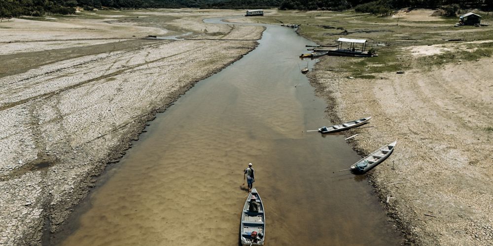 Un río con varios barcos flotando, mientras un hombre se encuentra en la orilla observando la escena.