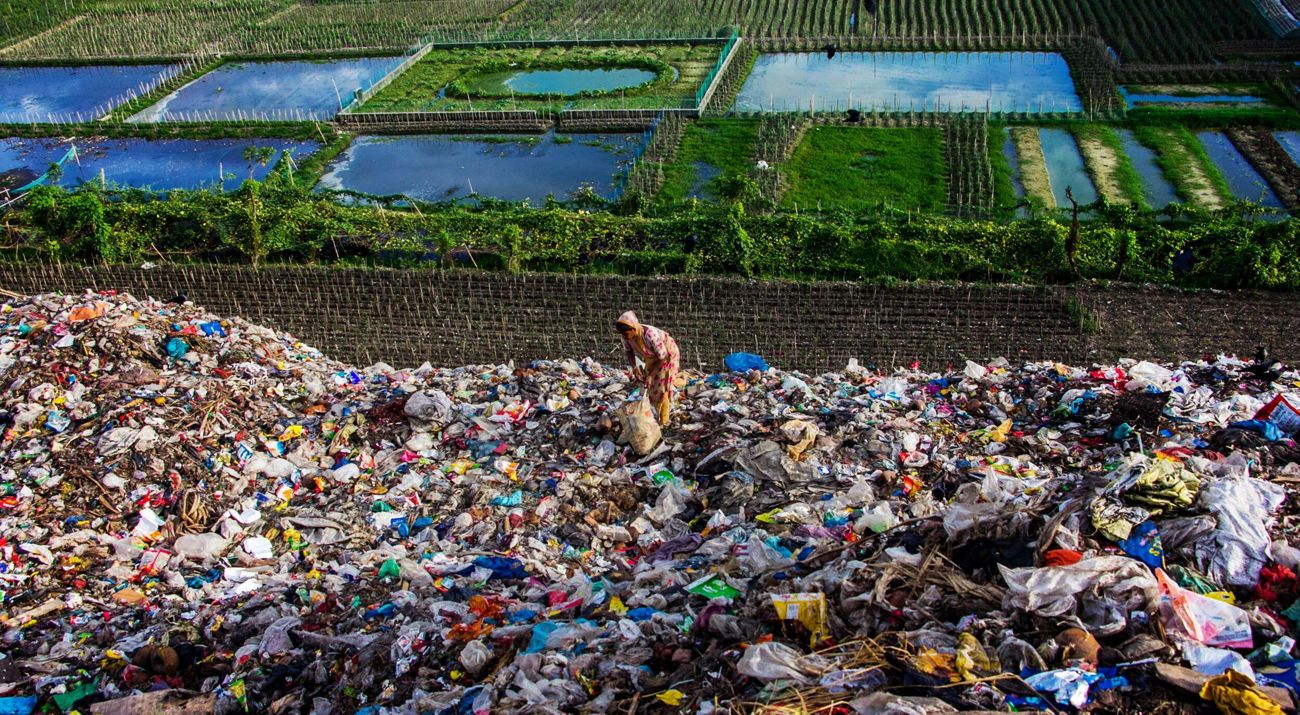 Mujer recogiendo basura rodeada por desperdicios.