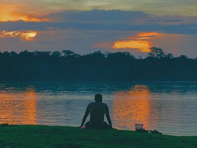 Hombre indígena mirando al horizonte a la orilla de un rio en el atardecer.