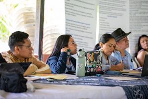 Un grupo de personas diversas sentadas alrededor de una mesa, cada una utilizando su ordenador portátil para trabajar o debatir en colaboración.
