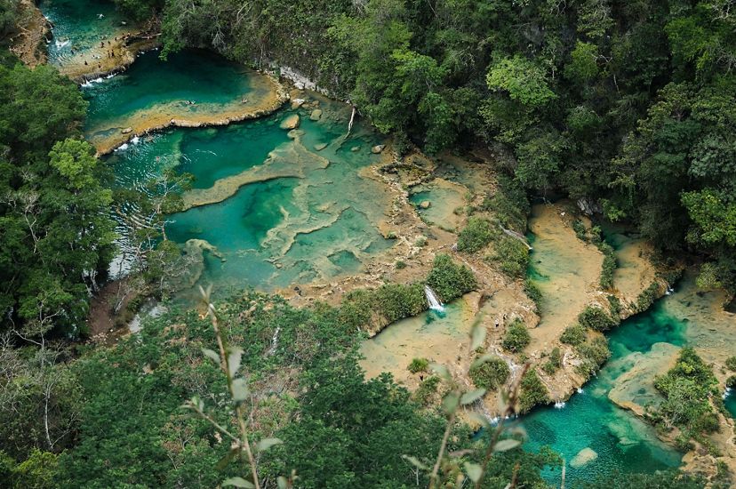 Aerial view of a series of naturally occurring pools of bright turquoise mineral water surrounded by forest