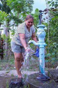 Una mujer vierte agua de una fuente azul en un recipiente, demostrando así el uso de la fuente.
