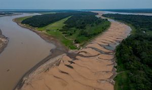 Vista aérea mostrando um rio sinuoso cercado por extensas dunas de areia sob um céu azul sem nuvens.