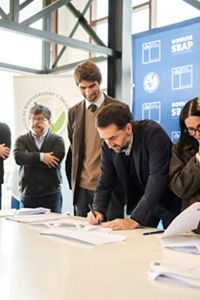 Un hombre de traje firma documentos en un escritorio, concentrado en el papeleo que tenía delante.