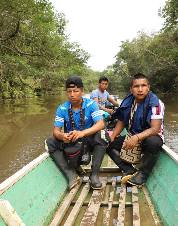 3 people sit in the back of a small boat on a river.