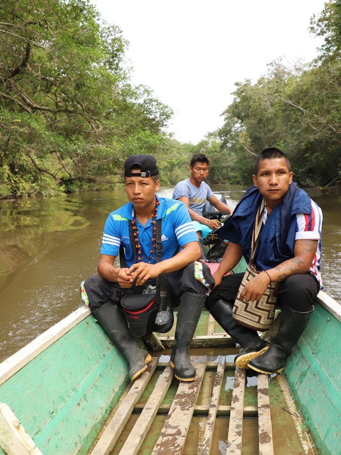 3 people sit in the back of a small boat on a river.