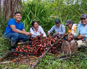Un grupo diverso de personas se sienta alrededor de una gran pila de frutas coloridas, conversando y compartiendo sonrisas.