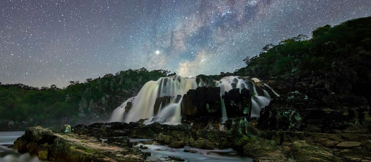 A waterfall rushes over rocky terrain under a starry sky.